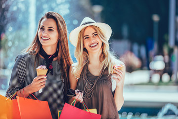 Happy young women with shopping bags and ice cream having fun on city street