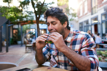 Young man sitting outside eating a delicious poppy seed bagel 