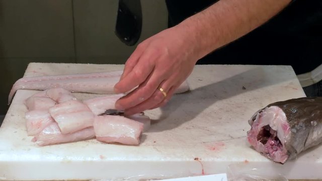 Shop owner cutting Fresh fish portions with a large knife.