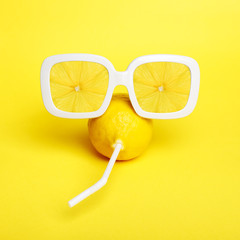Minimal tropic lemon in vintage sunglasses with straw on yellow.