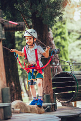 Little boy climbing in adventure activity park with helmet and safety equipment