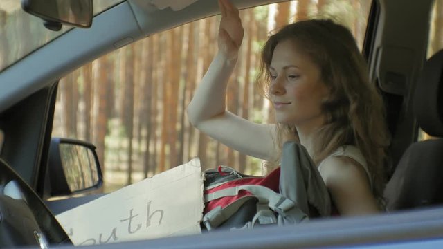 Young beautiful woman hitchhiking standing on the road with a backpack on a table with an inscription SOUTH in a car
