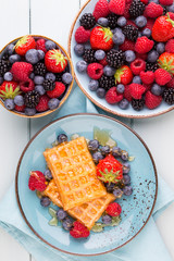 Homemade waffles with berries salad on blue dishes. Vintage wooden background.