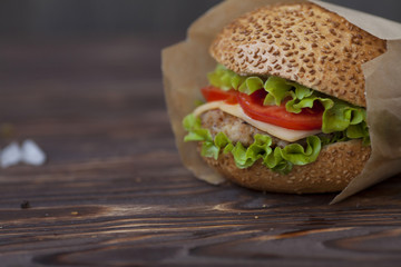 Burger with grilled beef, salad, cheese and tomato on dark background. Fast food. Craft burger on wooden background