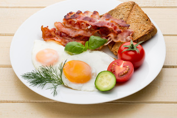 Fried eggs with bacon on the wooden table.