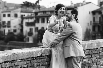 Groom holds bride sitting on the bridge of an old Verona