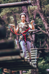 Happy school girl enjoying activity in a climbing adventure park on a summer day