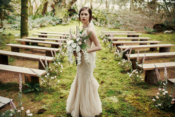 Worried bride stands between the benches in mystic forest