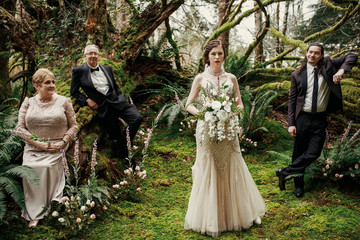 Bride, groom and their parents stand apart before an old tree posing in the mystic forest