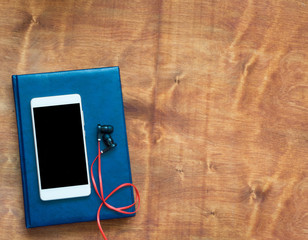Wooden table with smartphone, blue notebook and red earphones. Top view with copy space