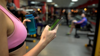 Fit girl scrolling pages on green phone screen during break in gym, application