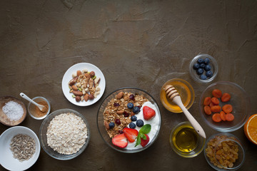 Ingredients for a healthy breakfast - granola, honey, nuts, berries, fruits, on dark olive background
