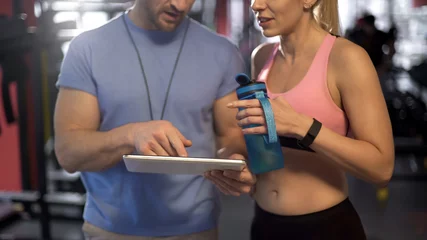 Foto op Plexiglas Sport woman discussing workout program with personal trainer, using tablet © motortion