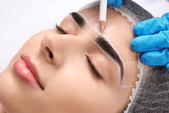 Cosmetologist preparing young woman for eyebrow permanent makeup procedure, closeup