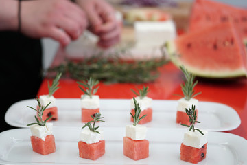 preparing watermelon and feta cheese cubes with rosemary. authentic greek cuisine with selective focus.