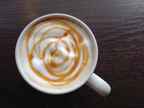 top view of caramel latte in coffee cup on dark wooden table