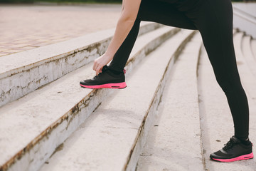 Cropped photo close up of female hands tying shoelaces on woman black and pink sneakers on training on stairs outdoors. Fitness, healthy lifestyle concept. Copy space for advertisement.