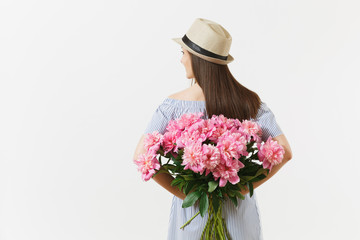 Young woman in blue dress, hat holding bouquet of beautiful pink peonies flowers behind her back isolated on white background. St. Valentine's Day, International Women's Day concept. Advertising area.