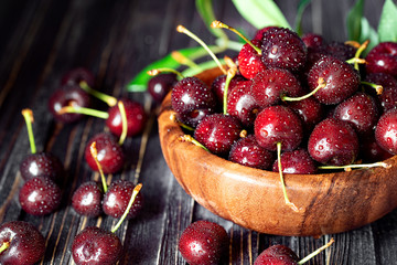 Fresh sweet cherries in plate on dark wooden background with copy space. Summer and harvest concept.