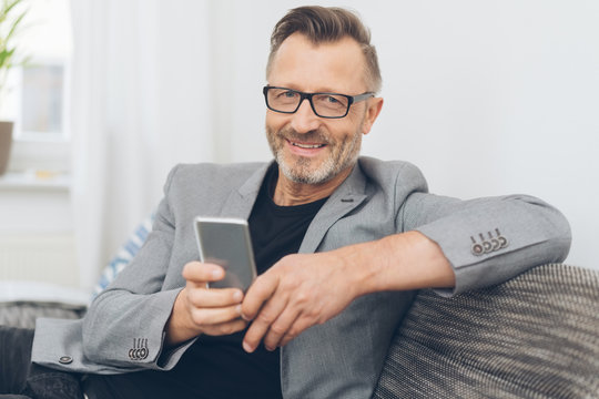 Smiling mature man sitting on sofa with phone