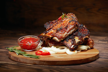 Fried ribs with rosemary, onion, sauce on a wooden round Board. Dark background. Place for text, copyspace