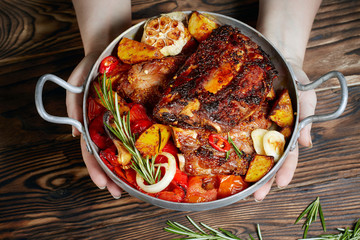 Hands holding fried ribs in a pan with rosemary, potatoes rustic, onion, sauce . Ribs are strung on a meat fork. Dark background. Place for text, copyspace