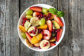 Fresh fruit salad, top view in a bowl on wooden background, vegetarian food concept