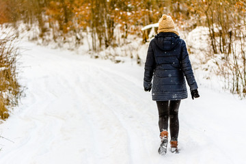 Woman in winter on snow road, girl in black coat, back view in park