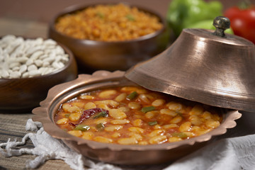 Dried beans,white beans in tomato sauce in a copper bowl closeup. horizontal
