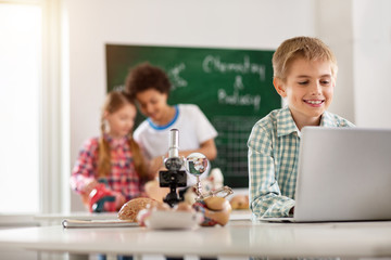 My project. Cheerful smart boy working on the laptop while working on his school project