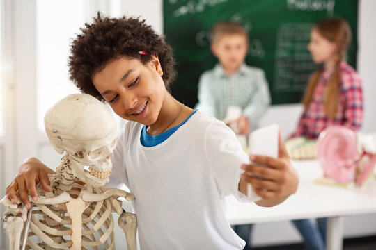 Positive emotions. Delighted nice boy smiling while taking a selfie with a skeleton