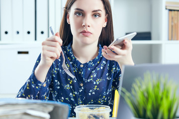 Business woman eating lunch at her workplace looking at the laptop screen. Folders with documents in the foreground. Dedline concept.