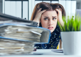 Tired and exhausted woman looks at the mountain of documents propping up her head with her hands. - 206966051