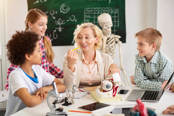 School teacher. Nice delighted woman sitting at the table while having a biology class