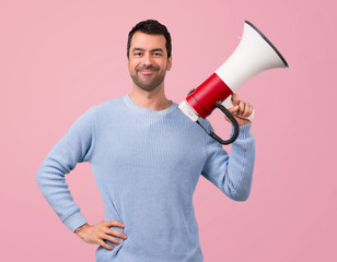 Man with blue sweater shouting through a megaphone on pink background