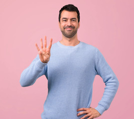 Man with blue sweater counting four with fingers on pink background