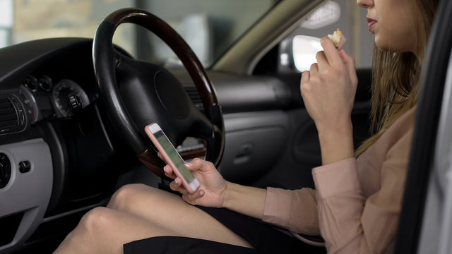 Female office worker sitting in car, eating sandwich and using smartphone - Powered by Adobe