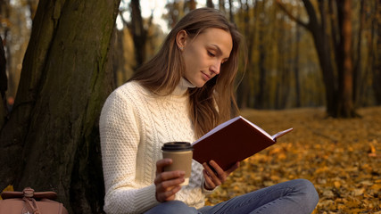 Obraz premium Female student reading book, sitting in beautiful park on warm autumn day