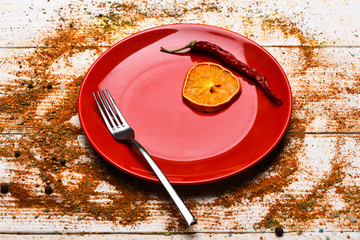 Culinary concept. Plate and fork with dried orange and chilly pepper on white wooden background....