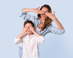 Mother and daughter covering eyes by hands on blue background