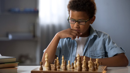 African American boy logically thinking out strategy of playing chess, hobby