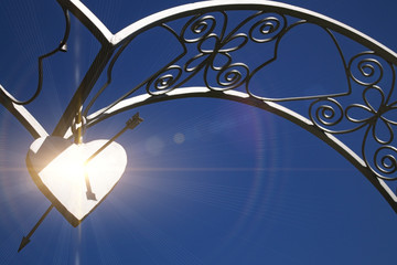 Arch with metal heart on the background of the sky and the rays of the sun