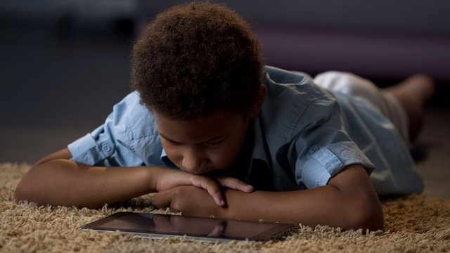 Lonely boy watching tablet movie lying on floor at home, lack of communication - Powered by Adobe