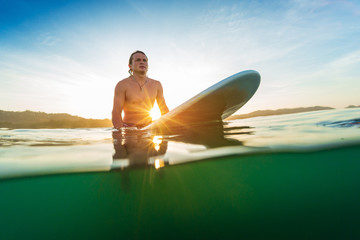 Young surfer waits a wave on line up at sunrise