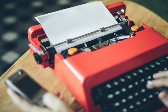 Hands holding cell phone and using typewriter