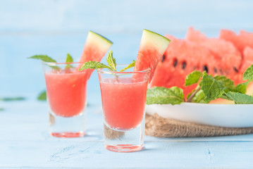 Cold watermelon smoothie drink in cocktail glass with slices of watermelon summer fruits on blue wooden background.