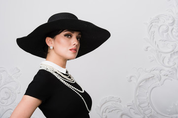 Portrait of a beautiful young woman in retro style in an elegant black hat and dress over luxury...