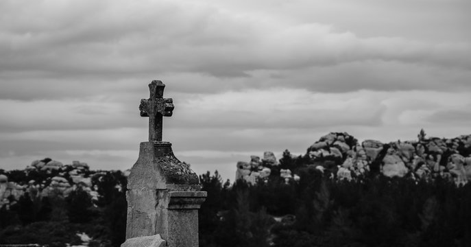 Tombstone with cross at old cemetery and rocky mountains at background (Provence, France). Black and white photo.
