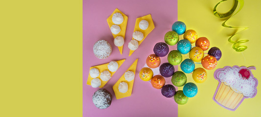 Top view of cake pops on a bright colorful yellow-pink background, decorated for birthday celebration, with bright yellow copy space. Selective focus