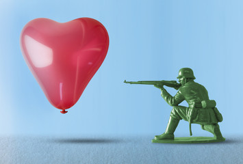 Heart balloon floating as a target for a toy soldier with gun representing the negative impact of...